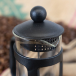 The lid on top of a small black cafetiere.